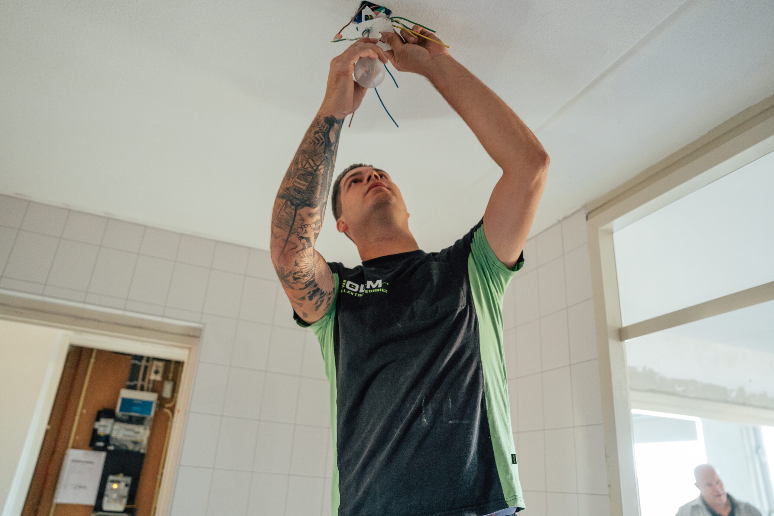Monteur van Van Olm sluit een lichtpunt aan in een woning, met de meterkast erachter.