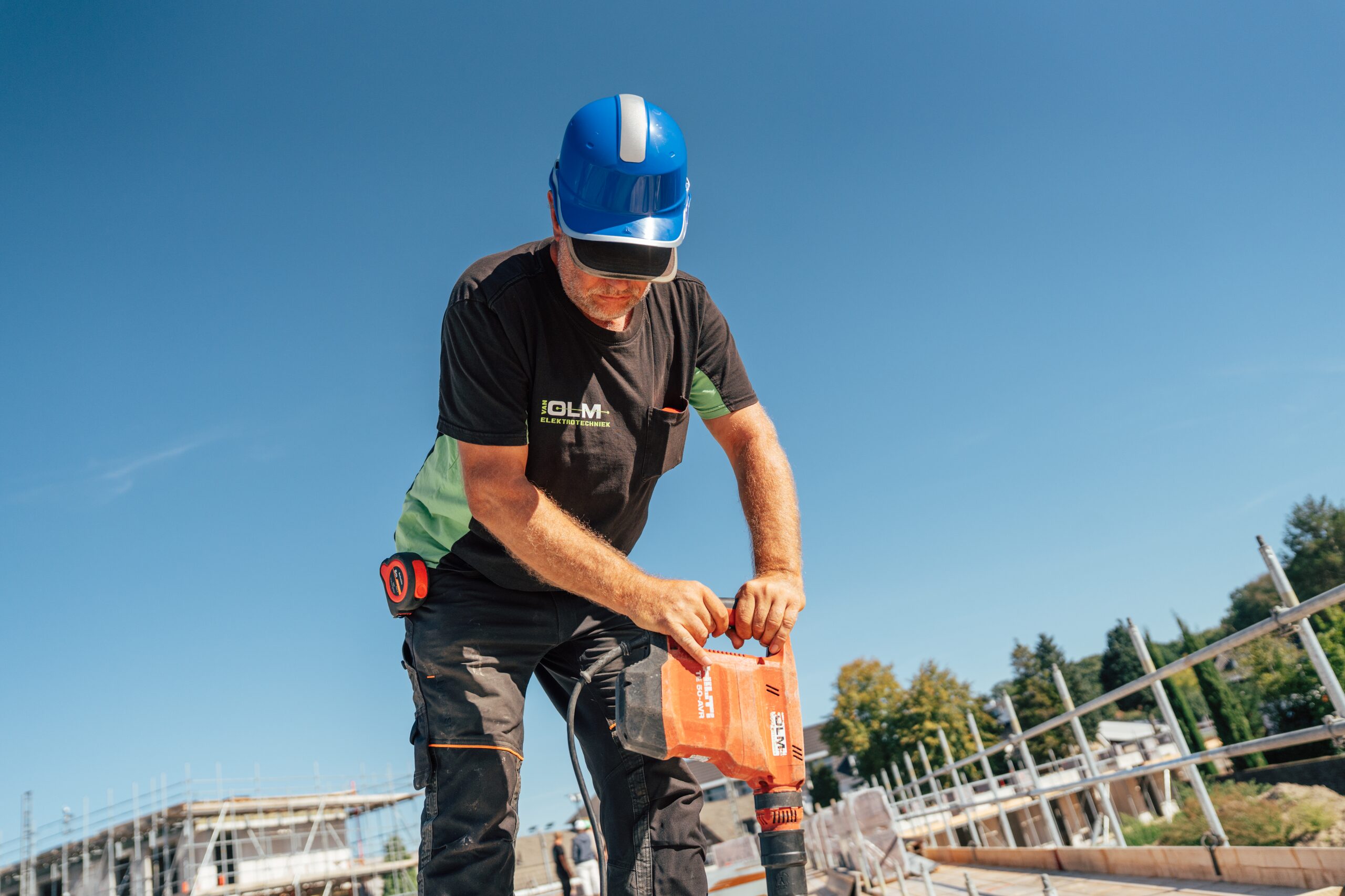 Monteur van Van Olm Elektrotechniek boort met een boorhamer in een betonvloer op een bouwplaats.
