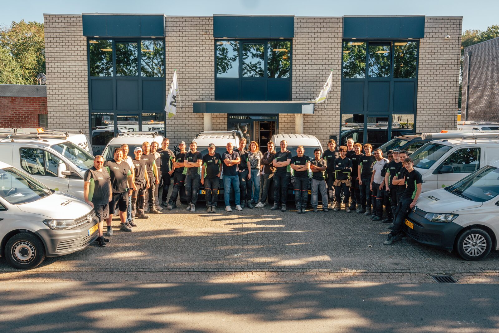 Het team van Van Olm Elektrotechniek tussen de witte bedrijfsbussen voor het pand in Oss.
