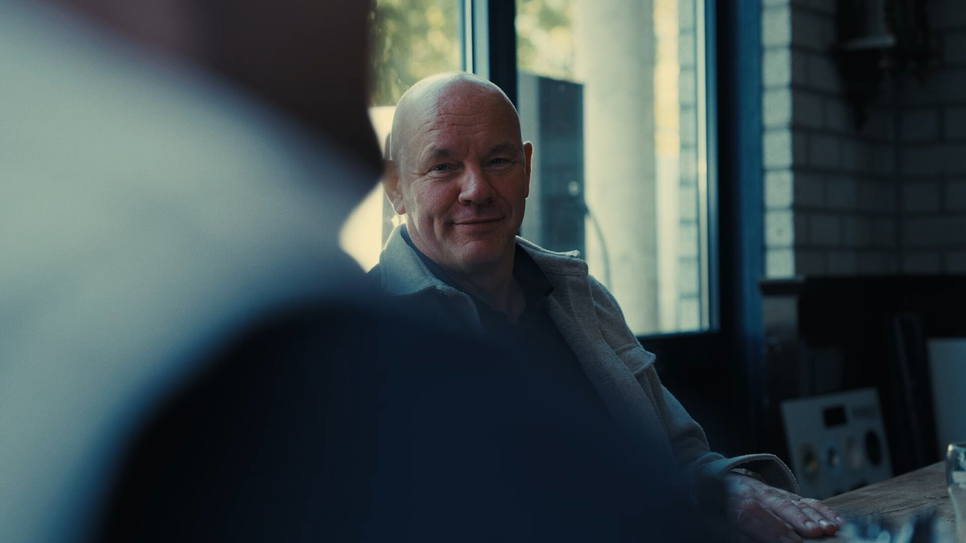 Collega in grijs jasje lacht aan tafel bij het raam.