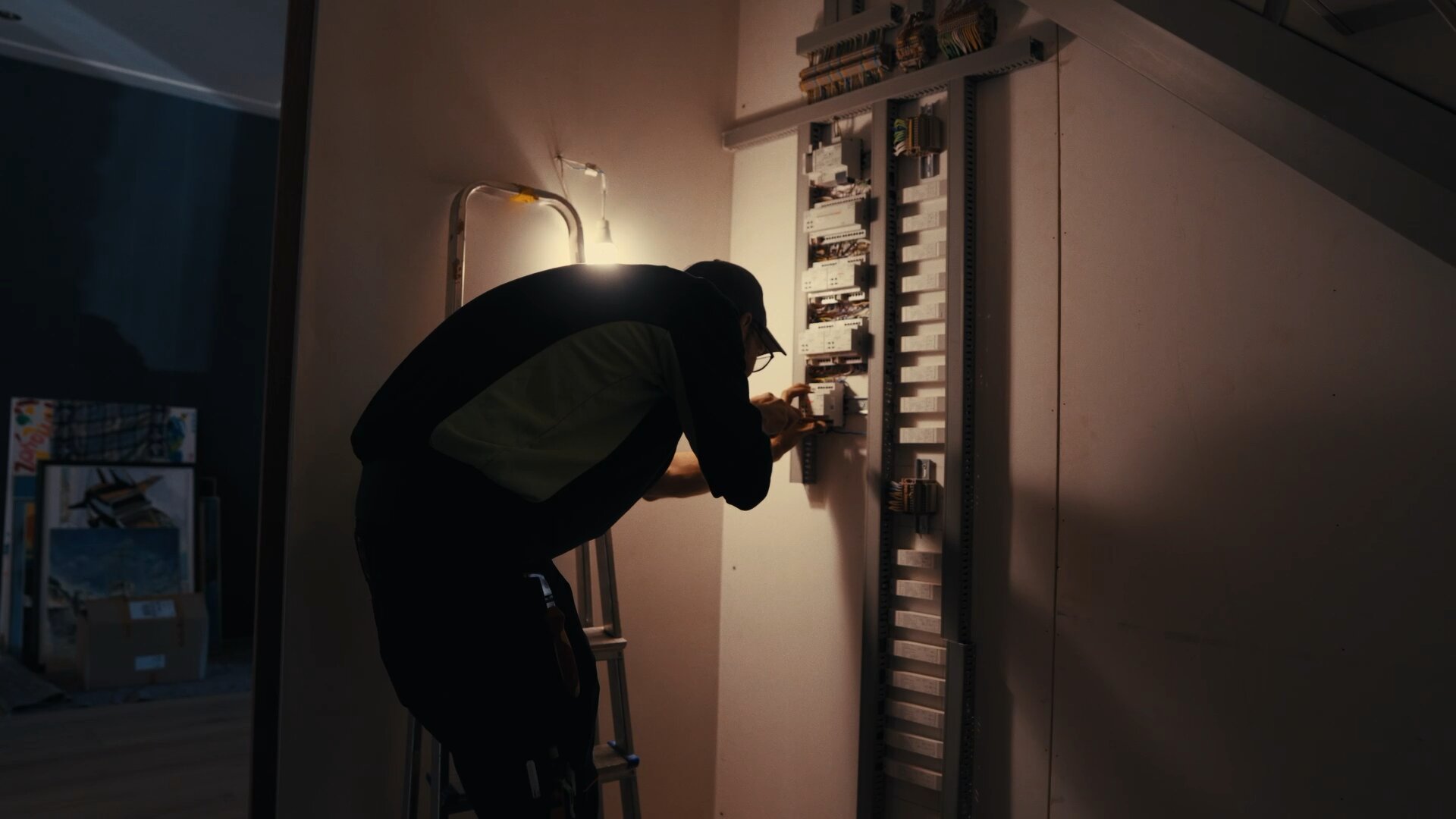 Monteur op een trap werkt bij lamplicht aan een verdeelkast in een woning.