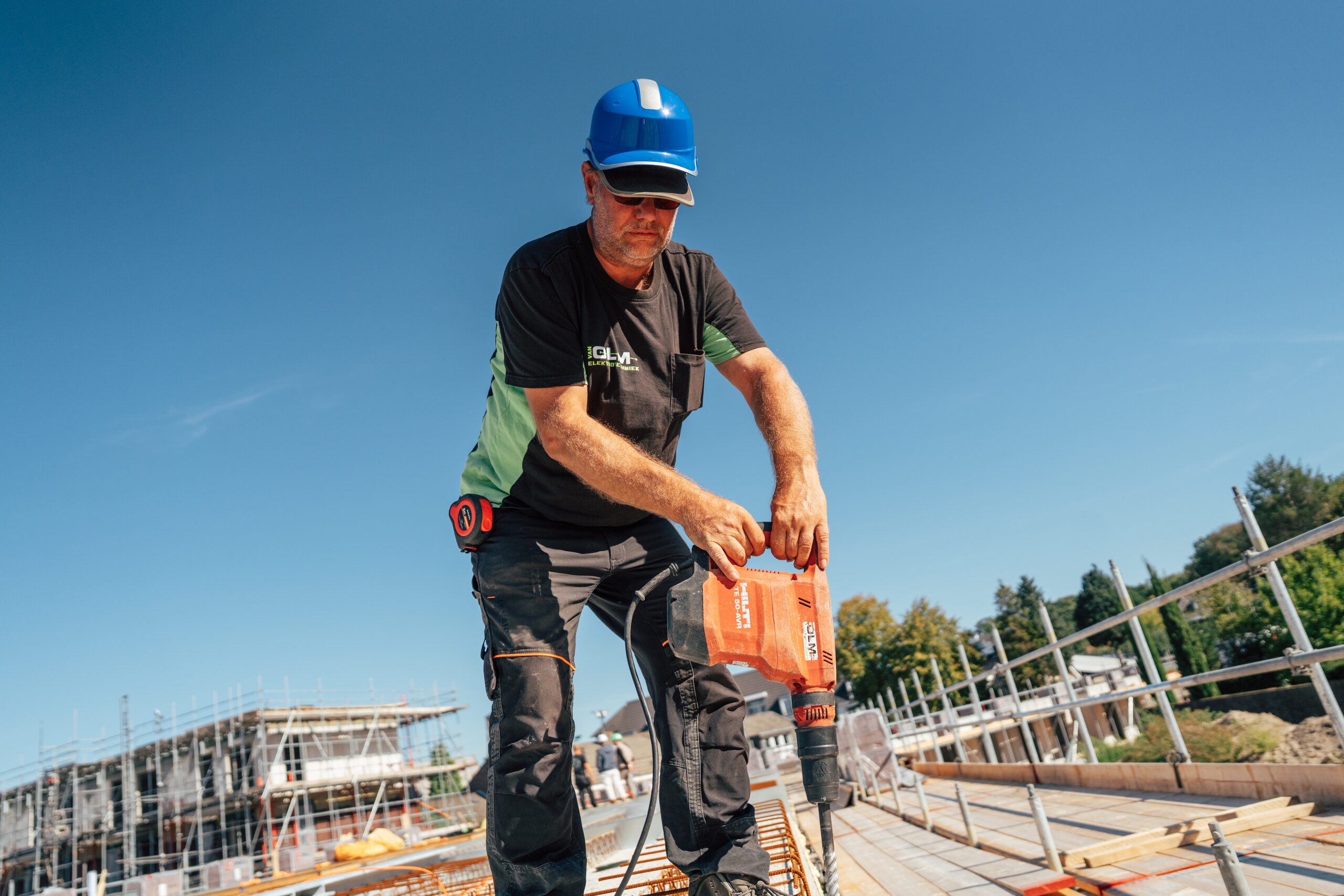 Monteur van Van Olm met blauwe helm boort met een Hilti-boorhamer op een betonvloer.