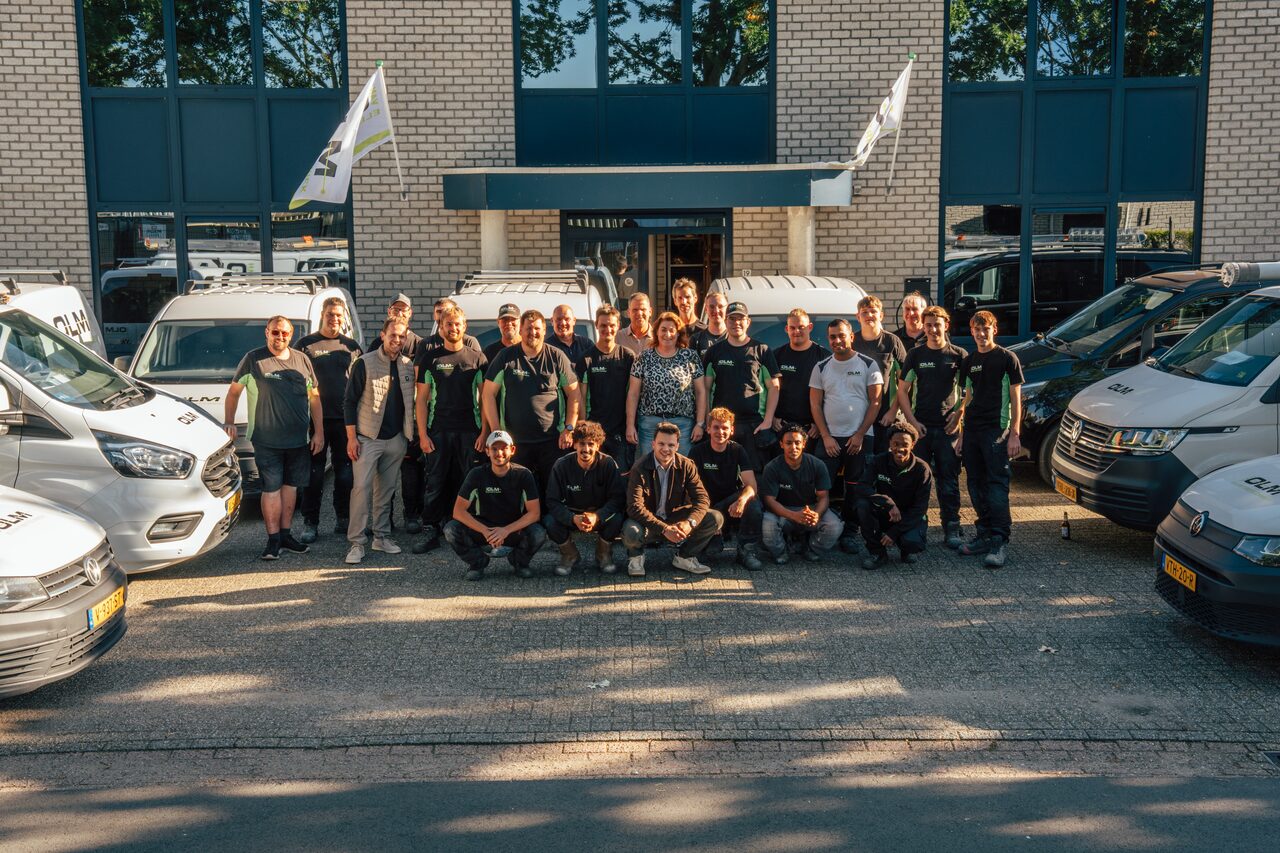Het team van Van Olm Elektrotechniek voor het pand in Oss, tussen de witte bedrijfsbussen.