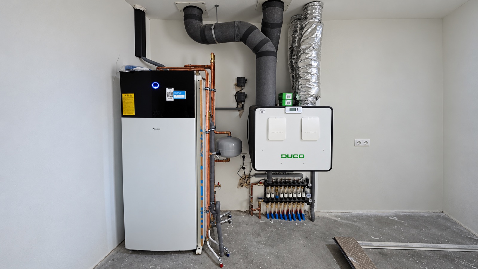 Daikin-warmtepomp naast een Duco-ventilatie-unit en een vloerverwarmingsverdeler in de technische ruimte.