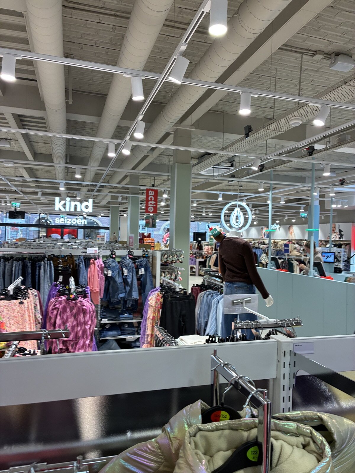 Witte railspots boven de kledingrekken in een winkel, met de borden ‘kind’, ‘seizoen’ en ‘actie’.
