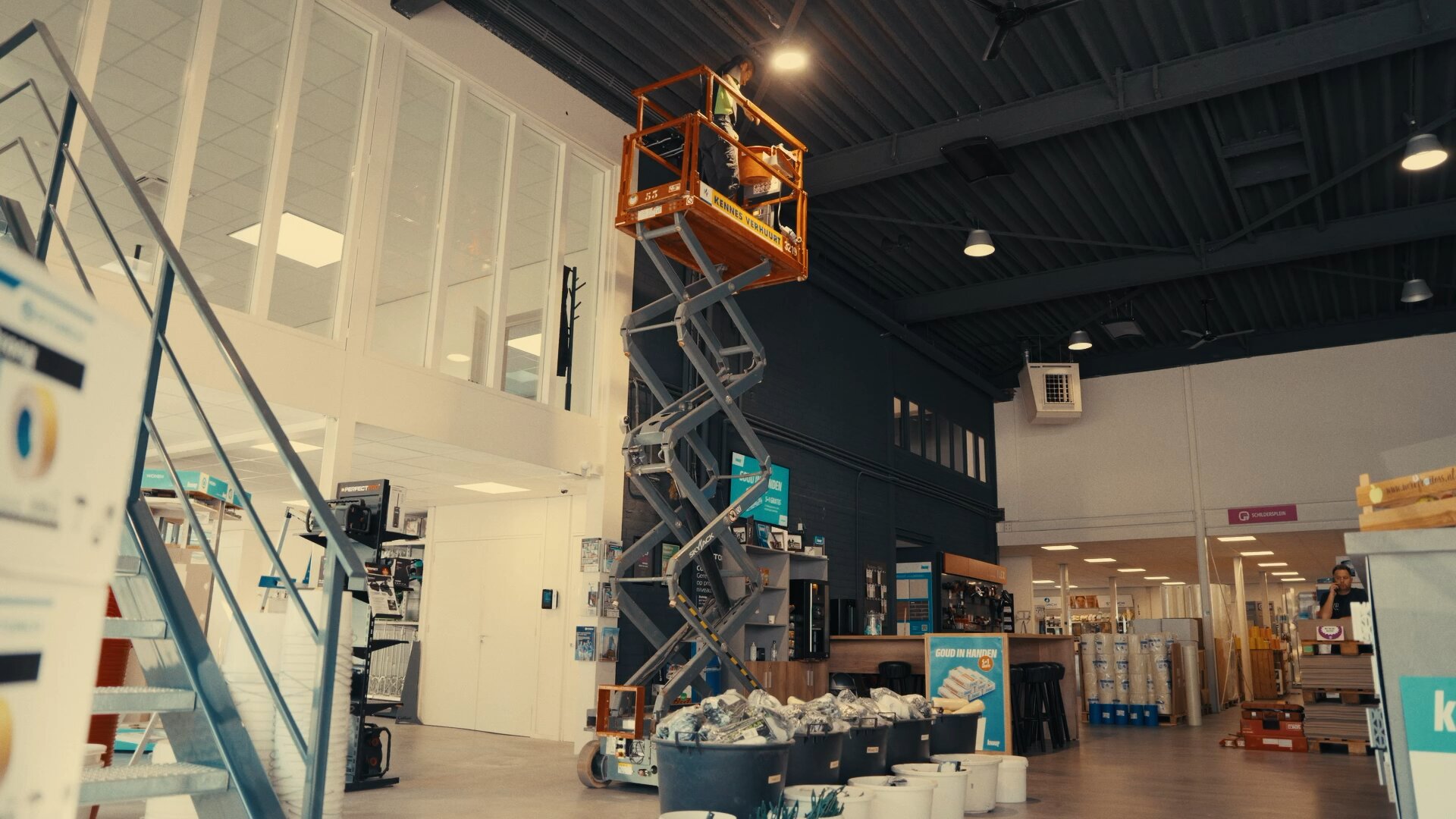 Monteur op een schaarhoogwerker werkt aan de plafondverlichting in een bouwmaterialenwinkel.