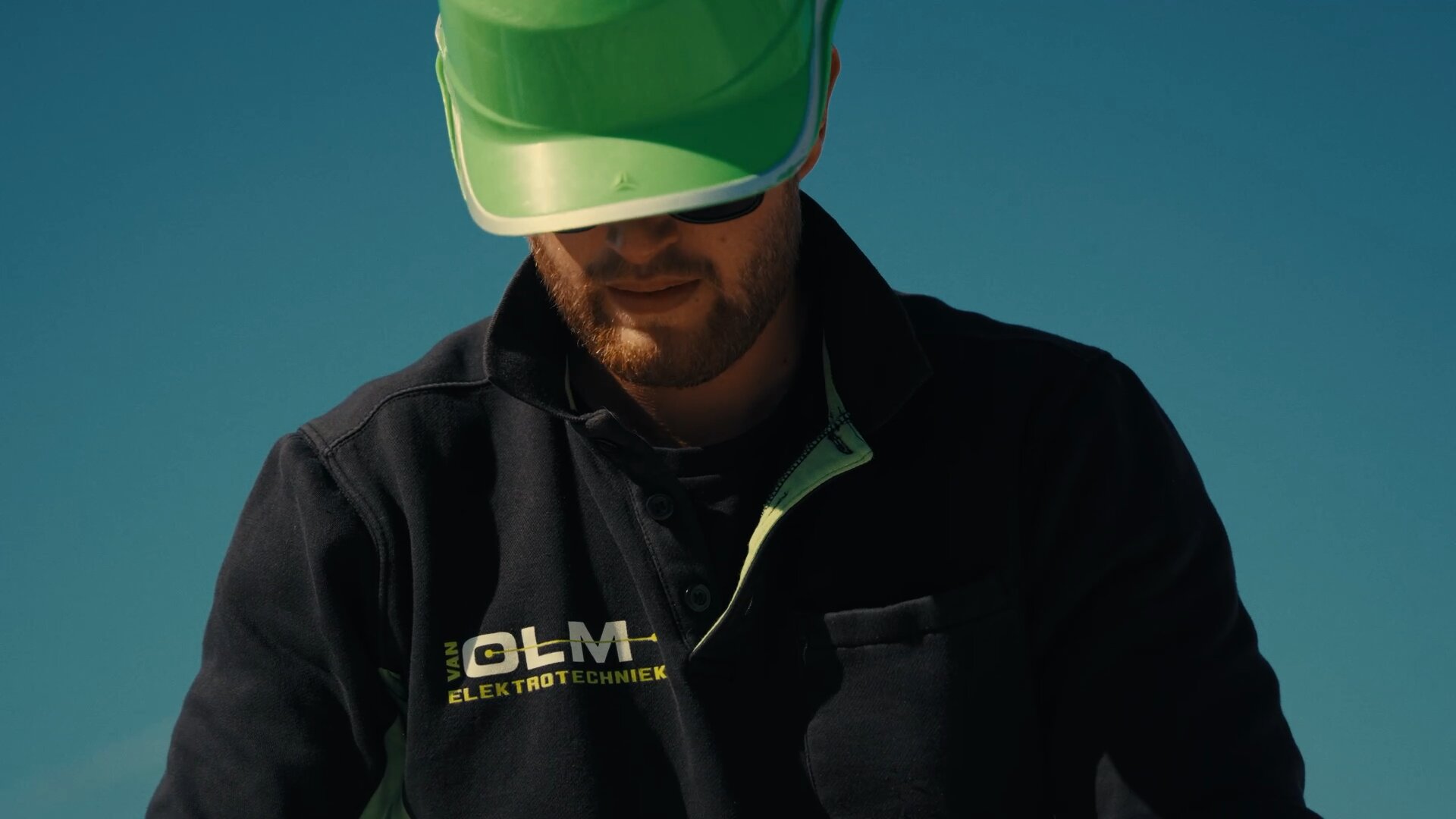 Monteur in werkkleding met het logo van Van Olm Elektrotechniek en een groene helm.