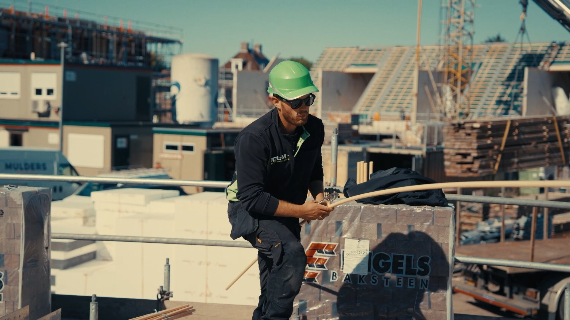 Monteur van Van Olm Elektrotechniek met een installatiebuis op de steiger bij nieuwbouwwoningen in aanbouw.