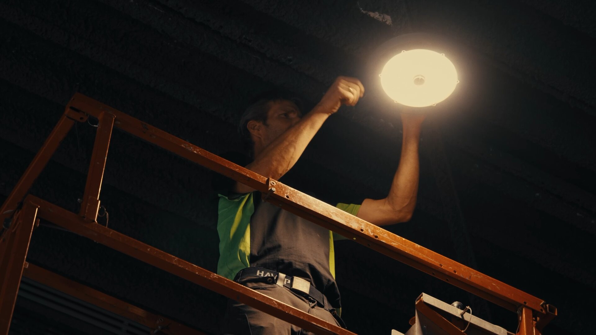 Monteur op een hoogwerker monteert een brandende ledlamp tegen het donkere plafond.